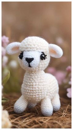 a small crocheted sheep sitting on top of some grass and flowers in the background