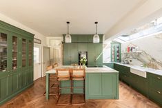 a kitchen with green cabinets and marble counter tops, wooden flooring and bar stools