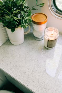 two candles and a potted plant sit on a counter top next to a window