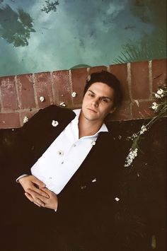 a man laying on the ground next to a brick wall with flowers in his lap