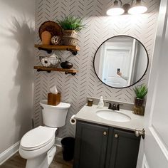 a white toilet sitting next to a sink in a bathroom under a round mirror on a wall