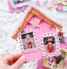 a hand holding up a pink house with two pictures on it and a star hanging from the roof