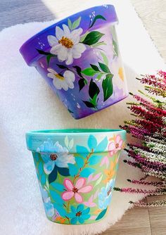 two flower pots sitting next to each other on top of a white rug with pink and blue flowers