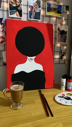 a cup of coffee sitting on top of a wooden table next to a painting with black hair