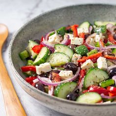 a salad with cucumbers, red onions and olives in a bowl next to a wooden spoon