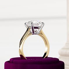 an engagement ring on top of a purple velvet stand in front of a white pillar