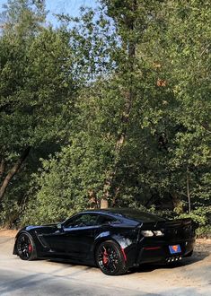 a black sports car parked on the side of a road in front of some trees