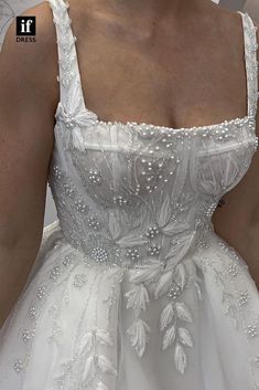 a woman wearing a white dress with beading on the bust and shoulder, in front of a mirror