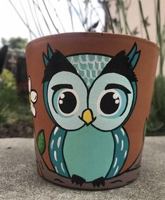 a pot with an owl painted on the front and sides, sitting on a cement surface