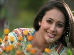 a woman laying in the grass with orange flowers around her neck and smiling at the camera