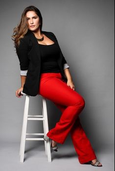 a woman sitting on top of a white stool wearing red pants and a black blazer