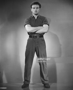 a man standing with his arms crossed and looking at the camera, in black and white