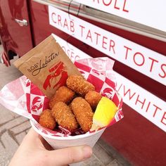 a hand holding a paper cup filled with tater tots next to a red truck