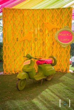 a green scooter is parked in front of a yellow wall with pink accents