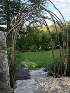 an arch made out of branches in the middle of a garden