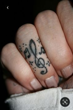 a person's hand with a musical note tattoo on their thumb and ring finger