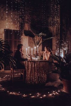 two women sitting at a table with candles in front of them, surrounded by potted plants