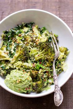 a white bowl filled with broccoli covered in pesto and topped with a fork