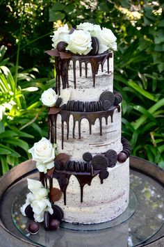 a three tiered cake with white flowers and chocolate drizzles on it