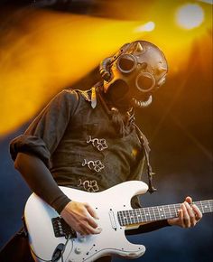 a man in a gas mask playing an electric guitar on stage at a music festival