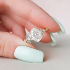 a woman's hand holding an oval shaped diamond ring on top of her finger