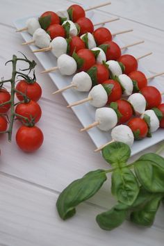 tomatoes and mozzarella skewers on a white plate next to basil leaves