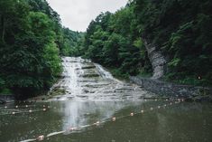 there is a small waterfall in the middle of the water with rocks and trees around it