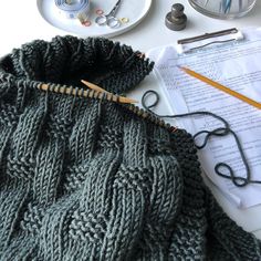 a knitted bag sitting on top of a table next to some scissors and yarn