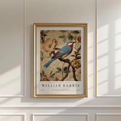 a blue bird sitting on top of a tree branch next to a framed poster in a room