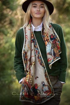 Woman wearing a green sweater, brown hat, and colorful scarf with bird designs outdoors.