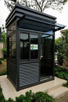 a small black and silver building in the middle of some bushes