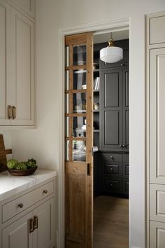 an open door leading to a kitchen with white cupboards and wooden shelves in it