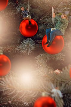 two people sitting on red ornaments hanging from a christmas tree