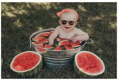 a baby sitting in a bucket with watermelon slices on the ground and wearing sunglasses