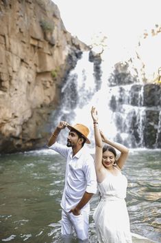 a man and woman are standing in the water near a waterfall with their arms around each other