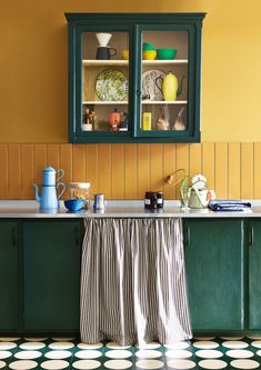 a kitchen with yellow walls and green cabinetry, black and white checkered floor