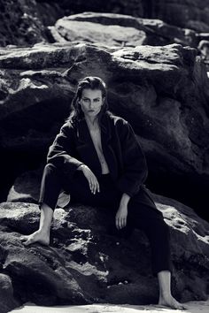 a woman sitting on top of a rock next to some rocks and water in black and white