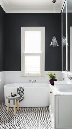 a white bath tub sitting under a window next to a sink and a mirror in a bathroom