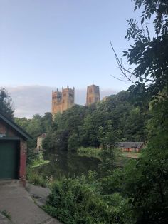 a river running through a lush green forest next to a tall building with towers on top