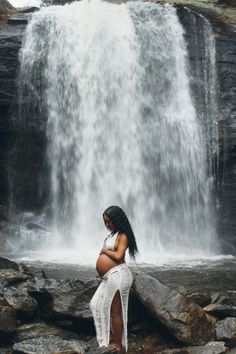 a pregnant woman standing in front of a waterfall