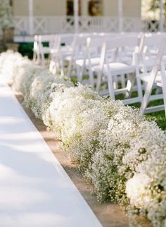 rows of white chairs lined up along the side of an aisle with flowers on it