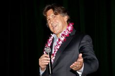 a man in a suit is holding a microphone and wearing a lei around his neck