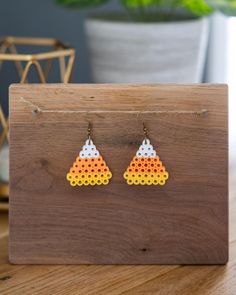 the earrings are made out of perforated wood and have white, yellow, orange, and red dots on them