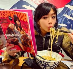 a woman eating noodles with chopsticks while reading the magazine nattibasi