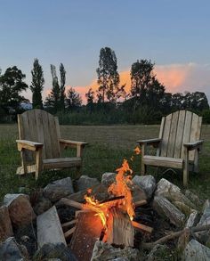 two wooden chairs sitting next to a fire pit in the middle of a grass field