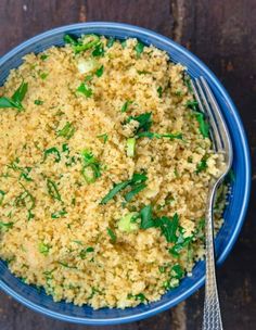 a blue bowl filled with rice and vegetables on top of a wooden table next to a fork