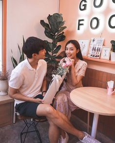 a man and woman sitting at a table in front of a plant with flowers on it