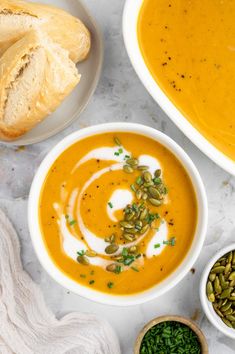 two bowls of carrot soup with bread and pumpkin seeds