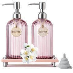 two pink soap dispensers with white flowers in front of them on a stand