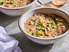 two white bowls filled with soup on top of a table next to crackers and bread